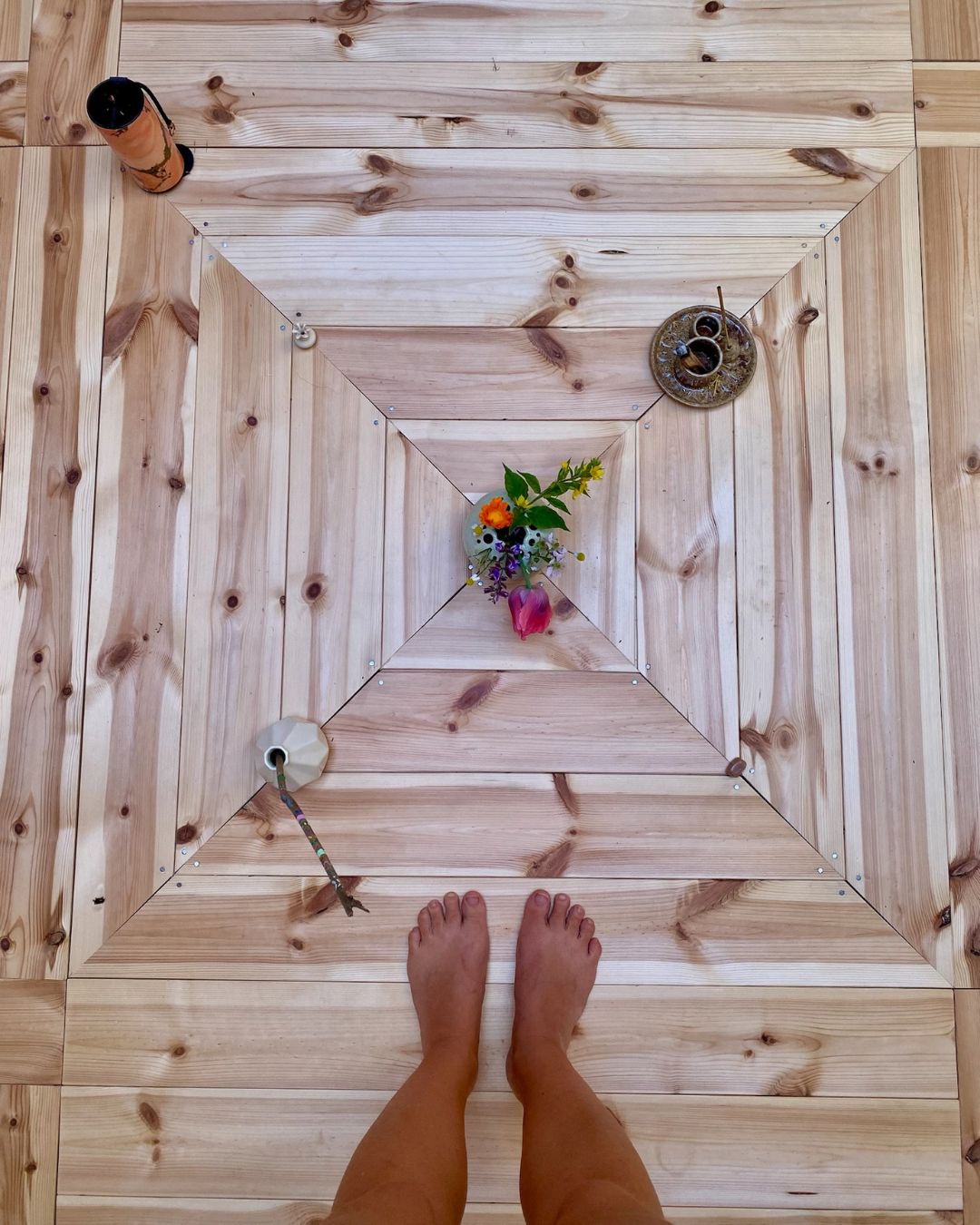Barfuß auf dem Holzboden der Jurte, davor ein kleiner Strauß Wildblumen und eine Kerze